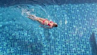 Cute woman in red swimsuit swim in swimming pool in sunlights on resort villa