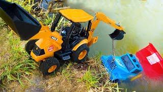 Трактор-экскаватор вытаскивает из пруда игрушечный грузовик который упал с моста