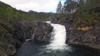 White waterfall into stone basin. Snowy mountains.