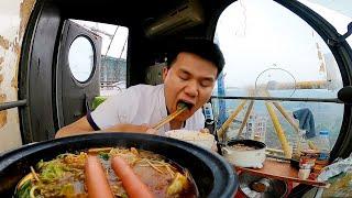 On a rainy day the tower crane driver eats hot pot and sings in the cab