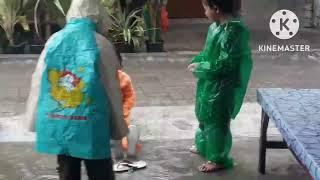 3 orang anak sedang asyiknya main hujan-hujanan bersama walaupun memakai jas hujan