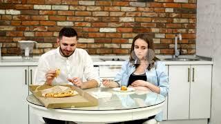 Man and pregnant woman eating pizza at home in their kitchen